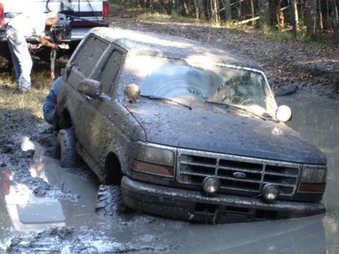 1989 Ford Bronco - This SUV is deeply stuck in the mud, with a person partially submerged trying to free it.