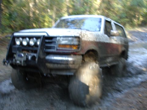 1989 Ford Bronco - This SUV, likely a 1992 Ford Bronco, navigates a muddy trail with a heavy-duty brush guard and winch.