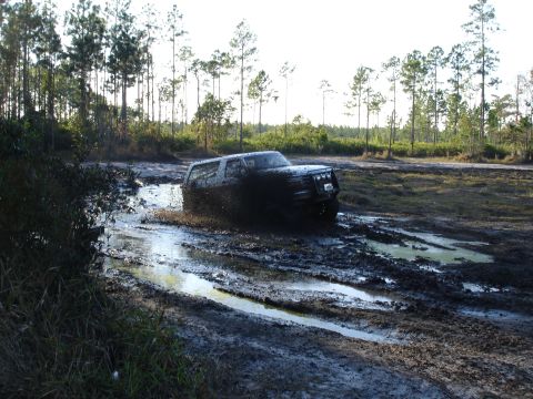 1989 Ford Bronco - A black SUV navigates a challenging muddy terrain, kicking up water and mud.