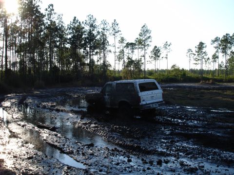 1989 Ford Bronco - A white 1989 Ford Bronco navigates a muddy track, its tires deep in the mire.
