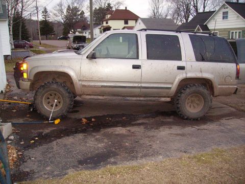 2000 Chevrolet Tahoe - Side view of a lifted 2000 Chevrolet Tahoe with off-road tires, appearing to be undergoing maintenance.