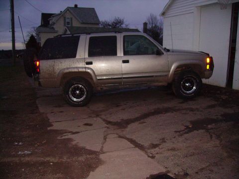 2000 Chevrolet Tahoe - A dirty Chevrolet Tahoe is parked on a wet driveway next to a white garage.