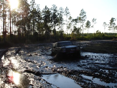 1989 Ford Bronco - An SUV navigates a challenging muddy terrain under a bright sun.