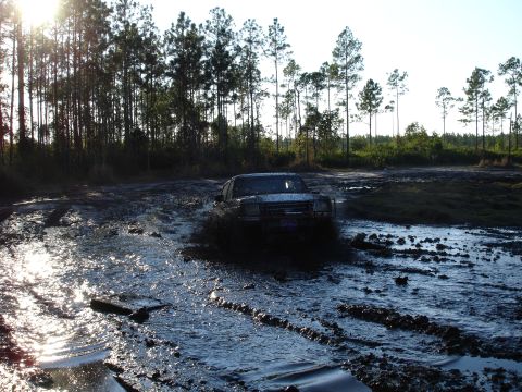 1989 Ford Bronco - A 1989 Ford Bronco navigates a muddy off-road course, kicking up a large spray.
