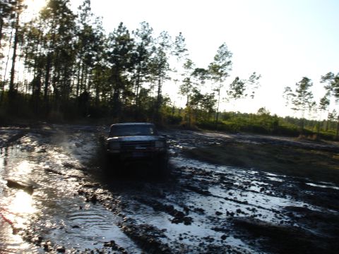 1989 Ford Bronco - A pickup truck navigates a challenging muddy terrain under a bright sky.
