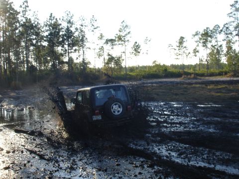 1989 Ford Bronco - Off-road Jeep Wrangler navigates a muddy track, creating a large splash.