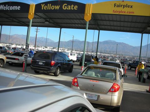 1998 Ford Crown Victoria - Vehicles queue at the Fairplex Yellow Gate entrance under a canopy, with attendants and a mountain backdrop in the distance.