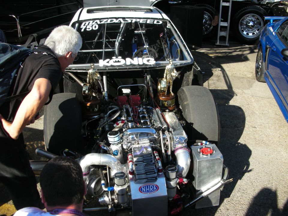 Exposed turbocharged engine of a black Mazdaspeed drag car in the pits