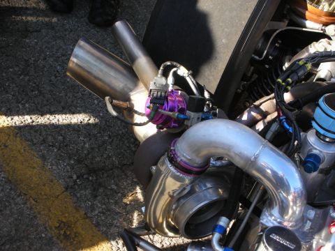 1998 Ford Crown Victoria - large polished turbocharger with a purple external wastegate and intercooler piping mounted on an engine, photographed over a parking lot.