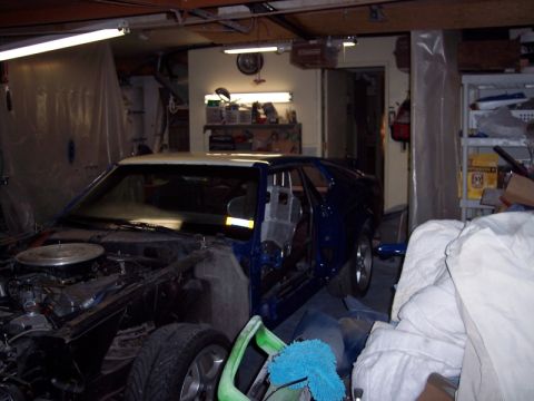 1971 Ford Mustang - A blue coupe is in a garage, with its hood removed and doors open, showing a stripped interior.