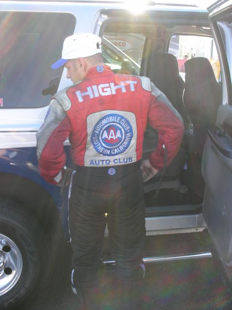 1998 Ford Crown Victoria - man in a red AAA Auto Club racing firesuit with HIGHT on the back steps into the open door of an SUV.