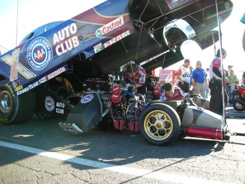 1998 Ford Crown Victoria - blue AAA Auto Club nitro Funny Car sits with its body raised, exposing the engine and gold wheels, in the pit area.