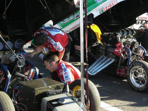 1998 Ford Crown Victoria - Two crew members in red team shirts work on the supercharged engine of a Funny Car in the pits.