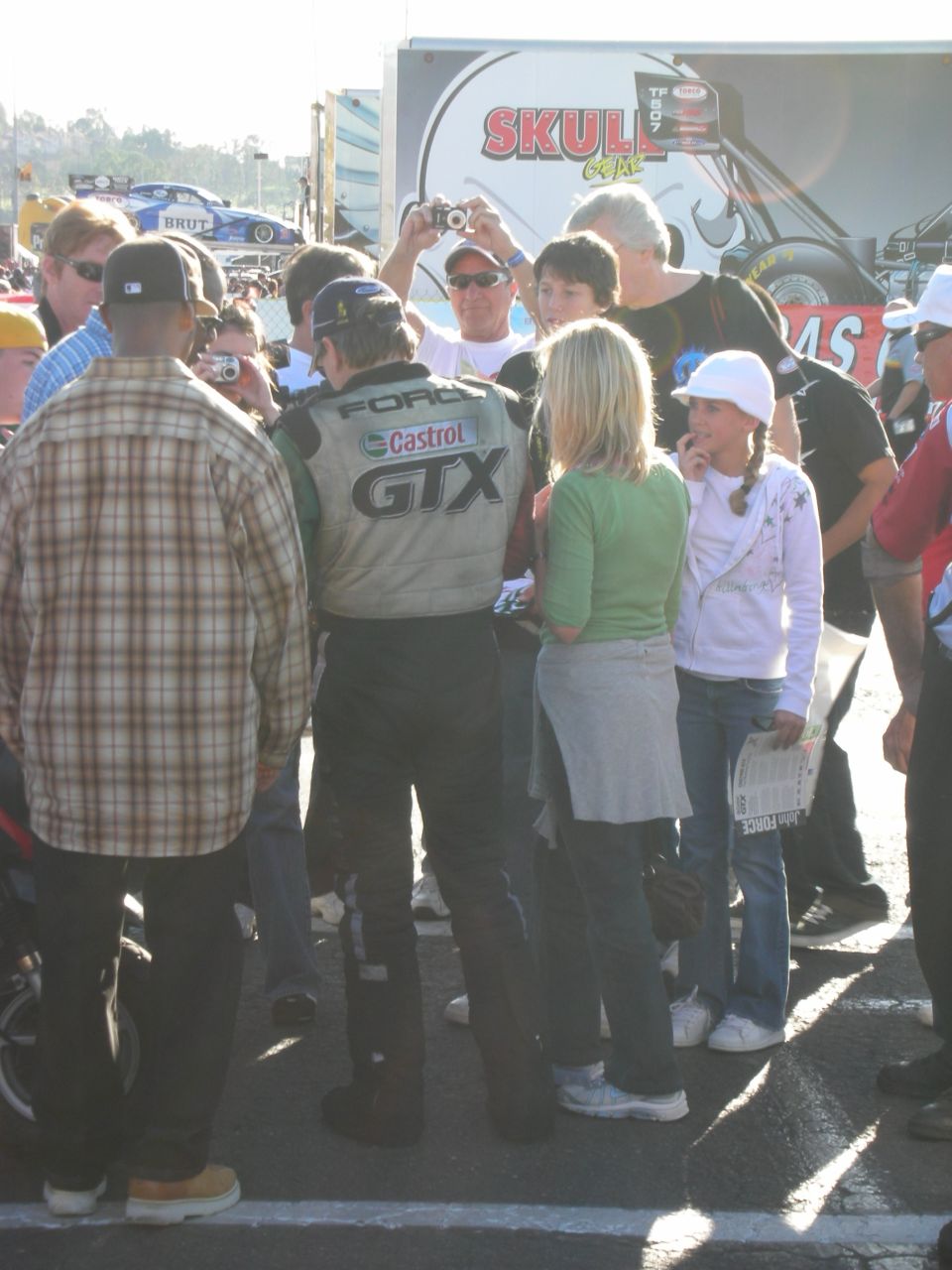 Crowd photographs a driver in Ford GTX firesuit near a Skull Gear booth