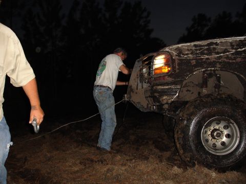 1989 Ford Bronco - A man attaches a rope to a muddy truck at night, likely to pull it out of a difficult situation.
