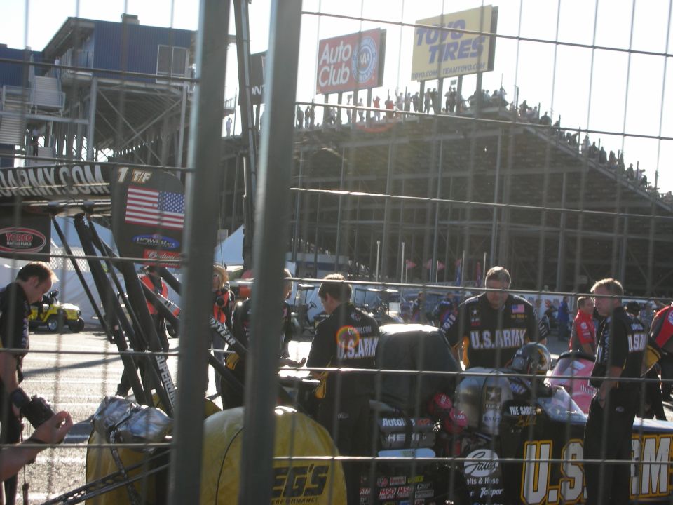 U.S. Army Top Fuel team in the pits with crew and grandstands behind