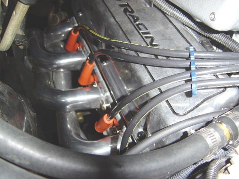 1986 Ford Bronco - Close-up down into an engine bay showing chrome shorty headers with orange spark plug boots and black plug wires routed over a cast intake…