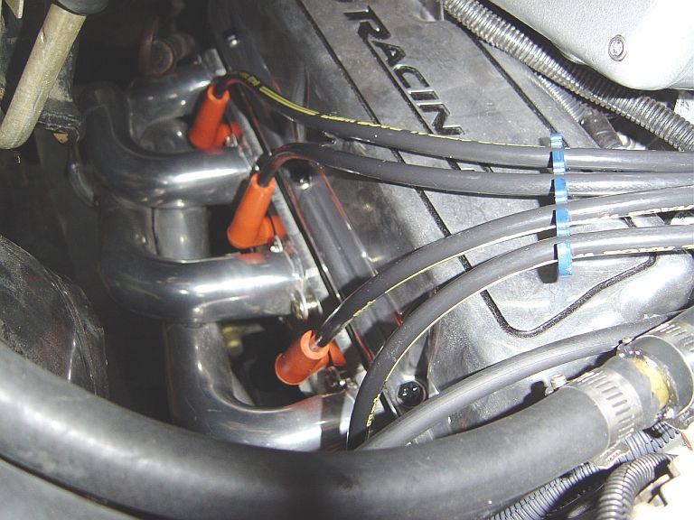 Chrome headers with orange plug boots and black wires over a RACING intake manifold