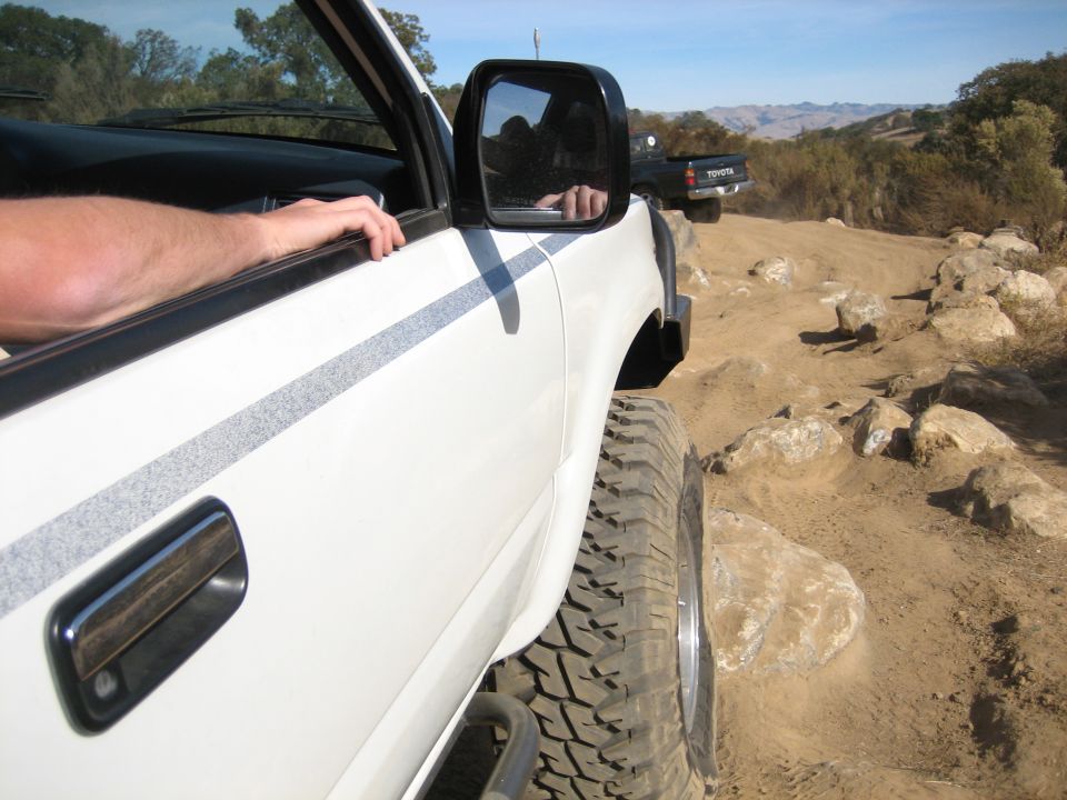 White Toyota pickup truck with off-road tires on a rocky dirt road