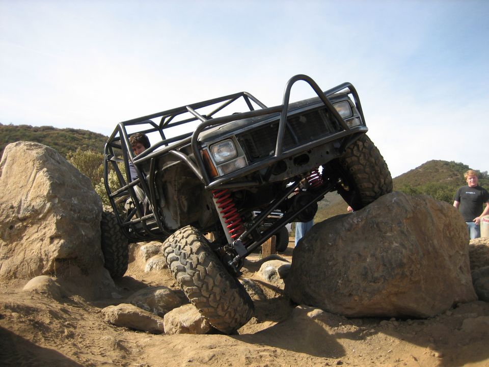 Black off-road vehicle with a roll cage, red shocks, and large tires, navigating large rocks