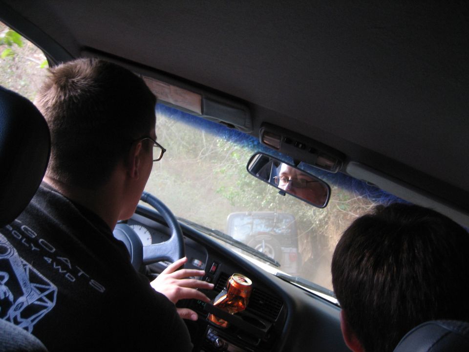 Driver and passenger inside a vehicle, looking out at another vehicle on a dirt road