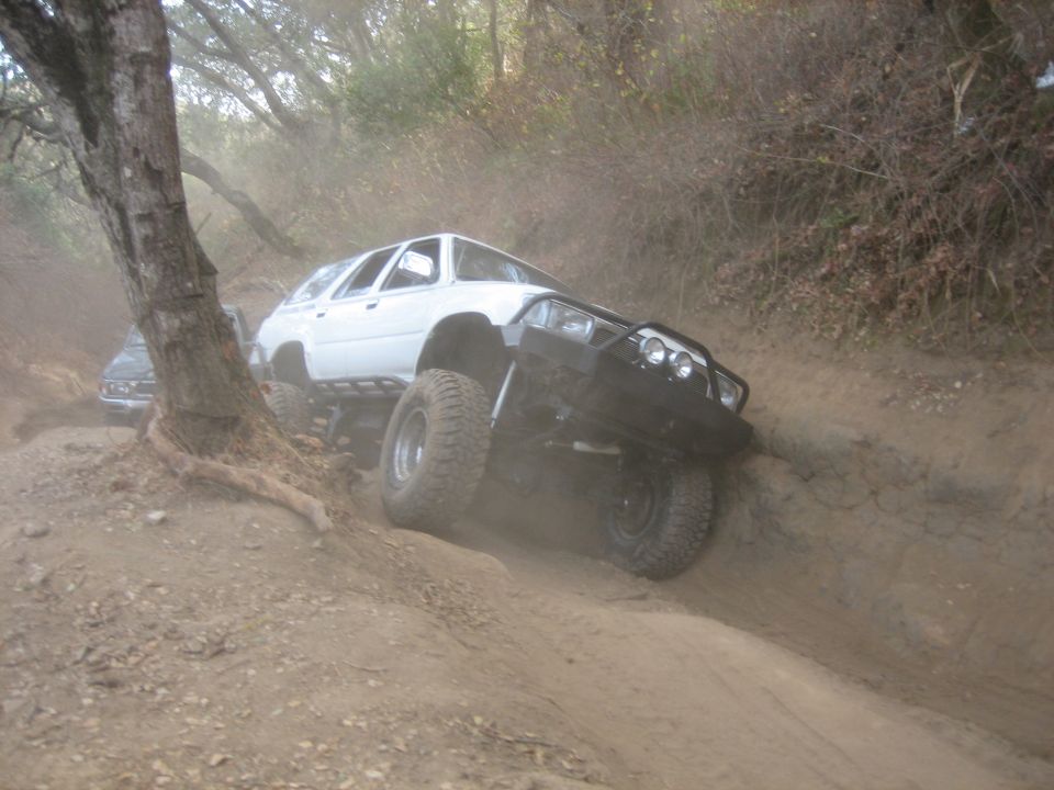 White 1993 Toyota 4Runner climbing a steep dirt trail with aftermarket bumper and large tires