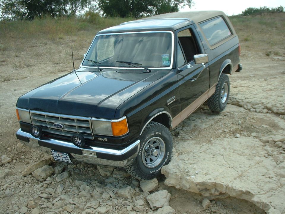 Black Ford Bronco 4x4 with tan trim and BFGoodrich tires parked on rocky ground, front three-quarter view