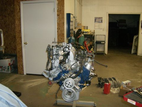 1992 Ford Bronco - A rebuilt V8 engine painted blue with fresh silver accessories sits on an engine stand in a workshop, with a front pulley and various remov…