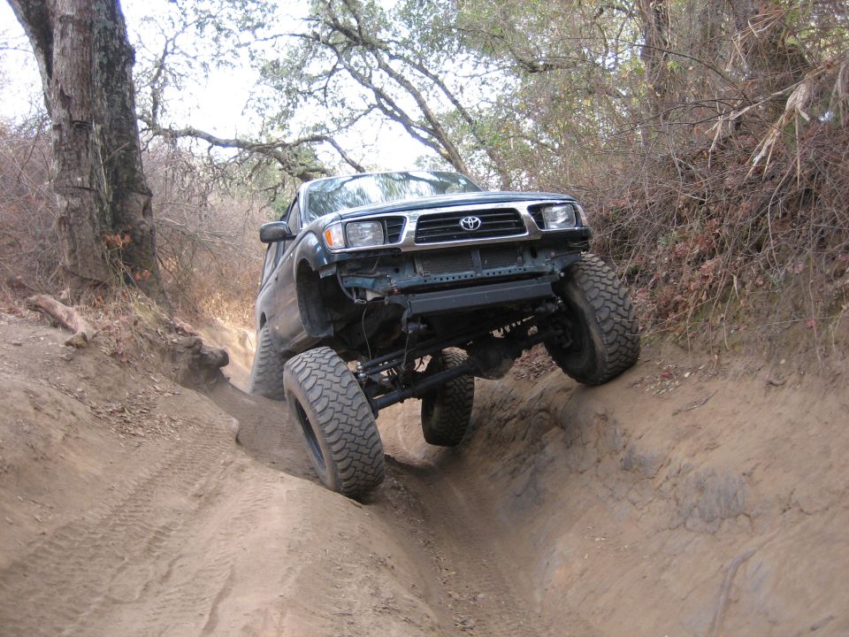 Toyota Tacoma with lifted suspension driving on a dirt trail, front bumper removed