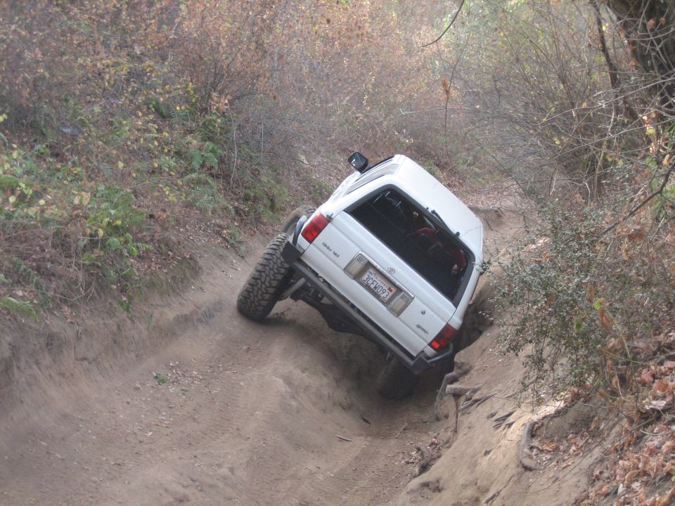 White SUV with lifted suspension navigating a steep dirt trail, tires angled