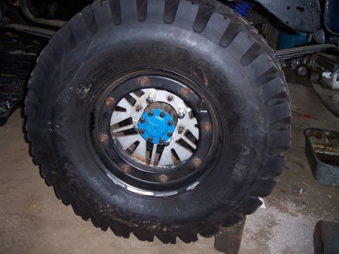 1983 Ford Bronco - Close-up of a large off-road tire and a custom wheel a bright blue hub and silver spokes.