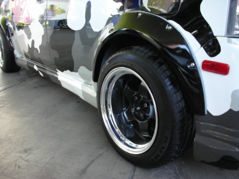 1998 Ford Crown Victoria - side and front wheel of a car wrapped in black-and-white urban camouflage, fitted with a black-and-polished alloy wheel.