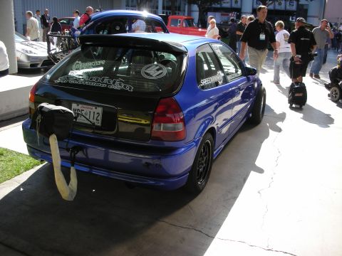 1998 Ford Crown Victoria - rear of a blue Honda Civic hatchback with stickers and a parachute pack, shown outdoors among a crowd at a car event.