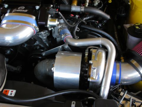 1998 Ford Crown Victoria - Detail of a supercharger, polished metal intake piping, and red cone filter packed into a tight engine bay.