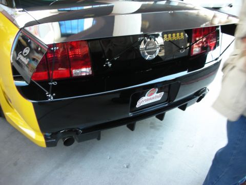 1998 Ford Crown Victoria - Rear of a black-and-yellow coupe showing twin tail lights, dual exhaust tips, and a Granatelli license plate.