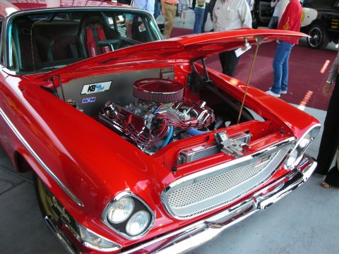 1998 Ford Crown Victoria - red vintage car with its hood open displaying a polished chrome V8 engine at an indoor car show.