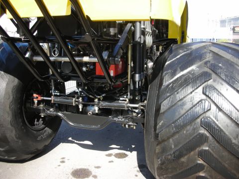 1998 Ford Crown Victoria - Underbody view of a yellow vehicle revealing suspension links, shocks, and a massive knobby off-road tire.