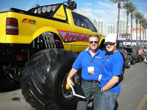 1998 Ford Crown Victoria - Two men in blue polo shirts pose beside a yellow Ford FX4 monster truck labeled Annihilator at an outdoor event.