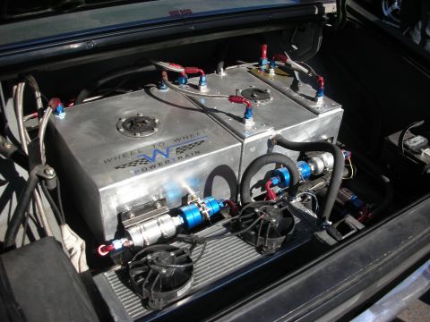 1998 Ford Crown Victoria - Two polished aluminum fuel cells with braided lines and pumps mounted in a trunk, labeled Wheel To Wheel Powertrain.