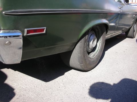 1998 Ford Crown Victoria - Close-up of the rear quarter panel, bumper, and worn tire of a faded green vintage car on pavement.