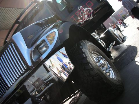1998 Ford Crown Victoria - Low-angle view of a black lifted truck's front clip, chrome fender, and large off-road tire under bright sun.
