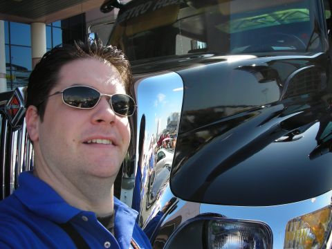1998 Ford Crown Victoria - smiling man wearing sunglasses and a blue shirt takes a selfie next to a shiny black truck outdoors.
