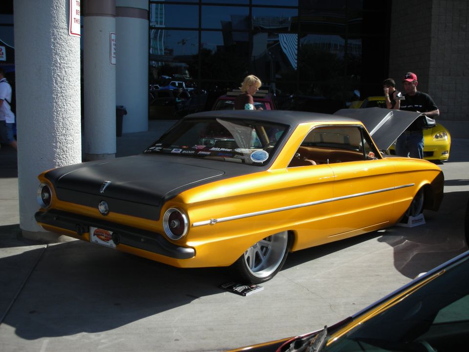 Gold-orange vintage coupe with black hood and white wheels at car show