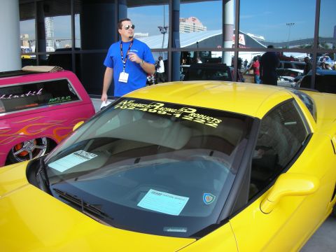 1998 Ford Crown Victoria - yellow sports car with vinyl lettering across its windshield as a man in a blue shirt stands by it indoors.