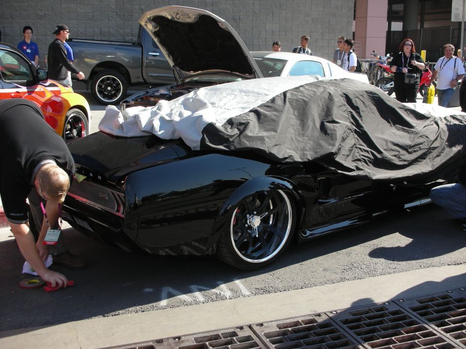 Black lowered car partly under a cover as a man details it outdoors