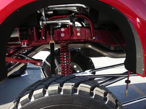 1998 Ford Crown Victoria - Undercarriage view of a lifted red truck with a chrome-and-red coilover shock, tubular links, and a knobby spare tire below.
