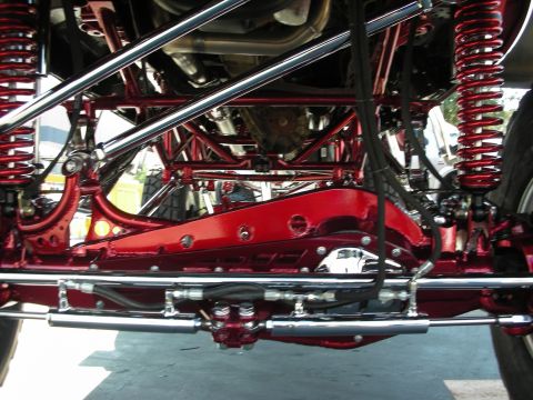 1998 Ford Crown Victoria - Close underside view of a custom truck's bright red chassis, chrome tubular links, polished shocks, and dual exhaust routing.