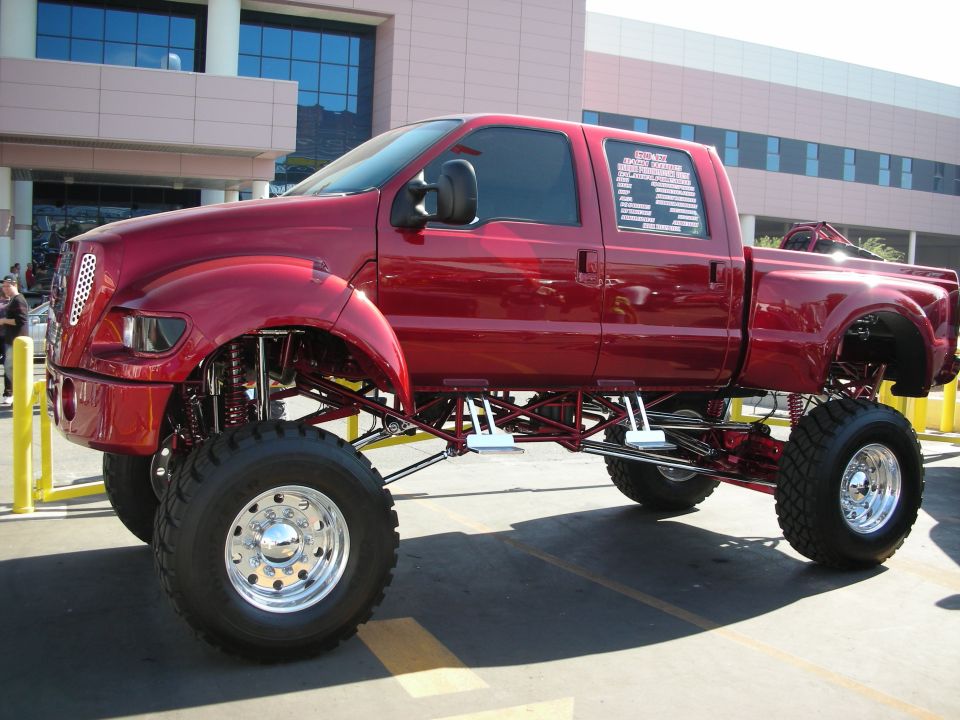 Candy-red lifted Ford crew-cab show truck on huge wheels in a parking lot