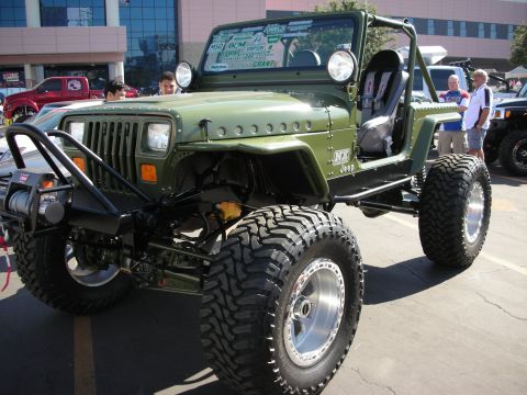 1998 Ford Crown Victoria - green Jeep Wrangler buggy with stripped body, tube fenders, winch bumper, and tall off-road tires displayed at a show.
