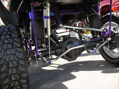 1998 Ford Crown Victoria - Underside view of a lifted truck's solid rear axle with purple painted links, reservoir shocks, and air springs.